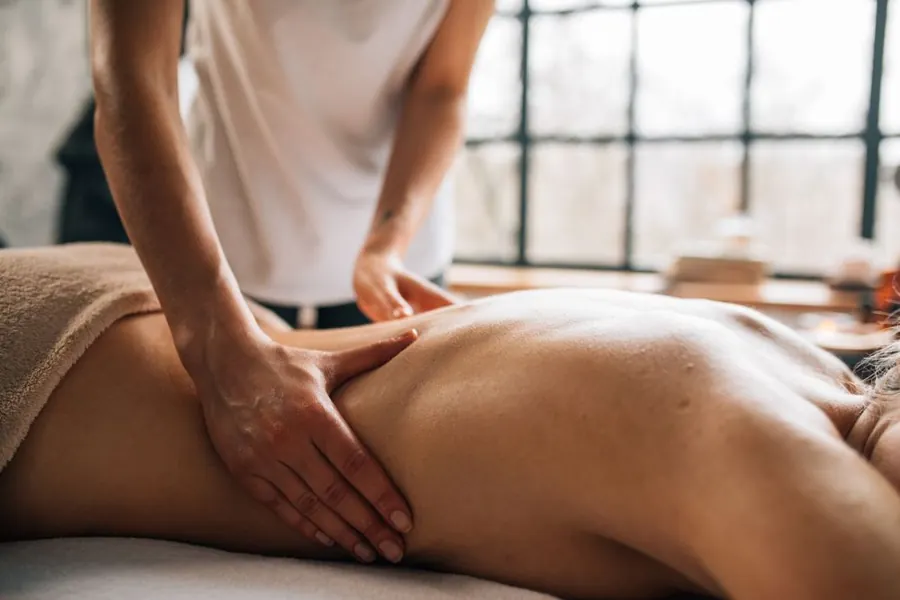 Hands performing a back massage in a bright treatment room